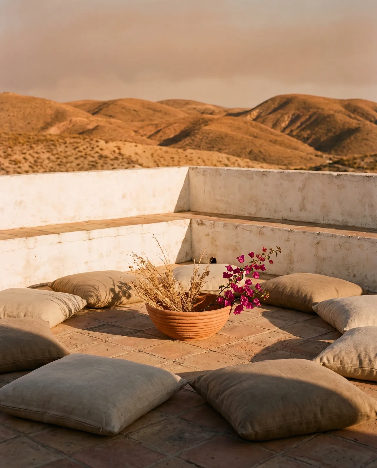 Terraza encalada frente a las lomas del desierto, con cojines de lino en el suelo