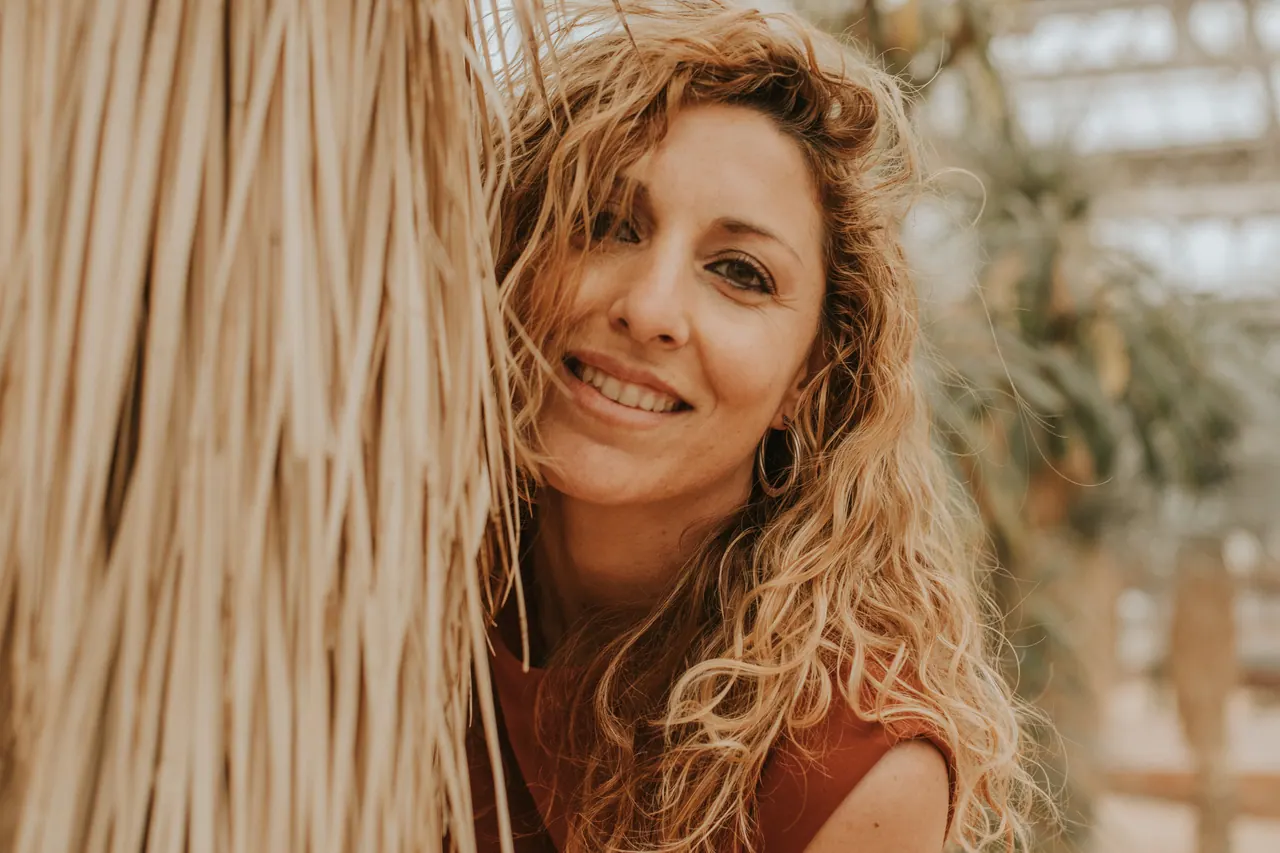 Carmen sonríe a cámara asomada junto al tronco de una palmera