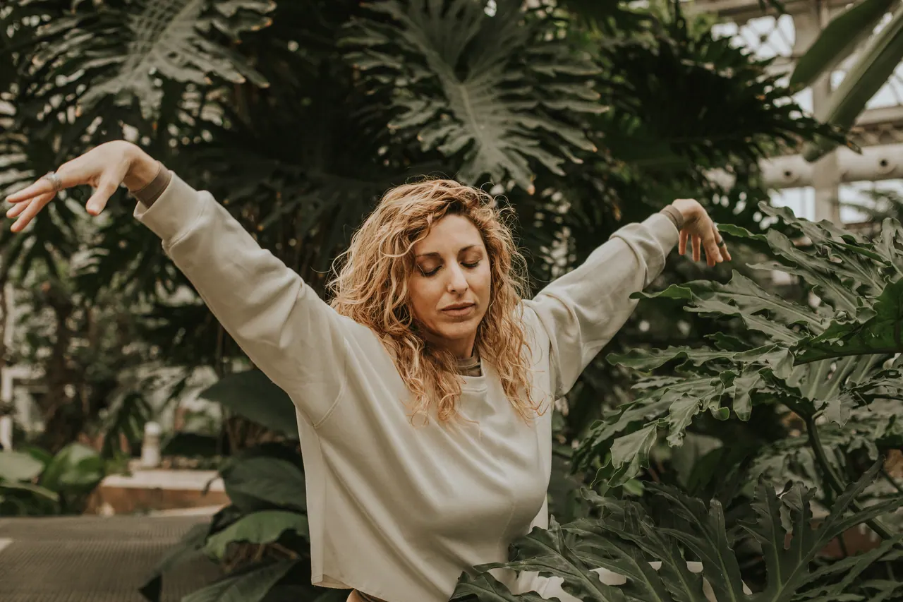 Carmen abre los brazos con los ojos cerrados, entre las plantas del invernadero