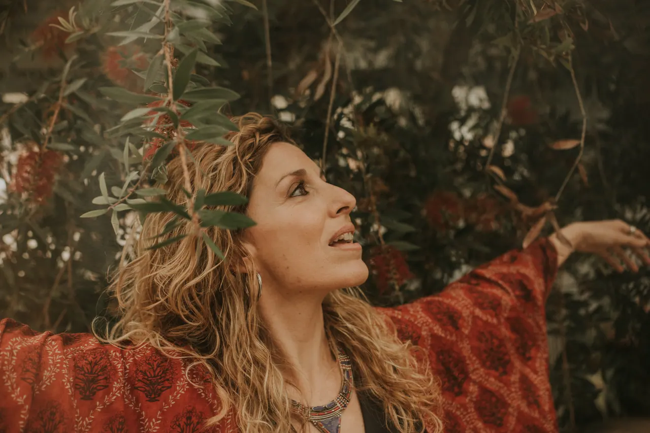 Carmen mira hacia arriba, con un kimono rojo, entre las plantas