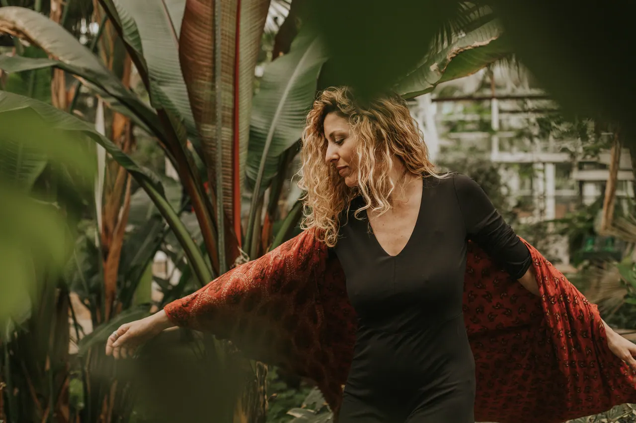 Carmen bailando entre las plantas con un kimono rojo abierto sobre un vestido negro